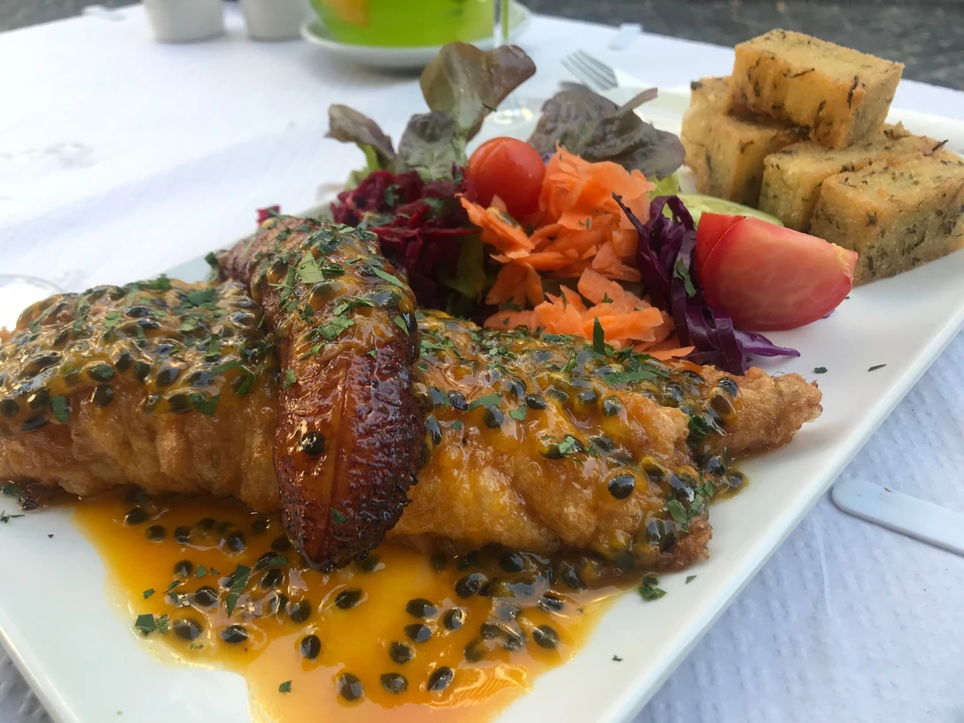 Gericht mit gebratenem Fisch in Passionsfruchtsauce, Salatbeilage, Kochbanane und gebratenem Brotwürfel.