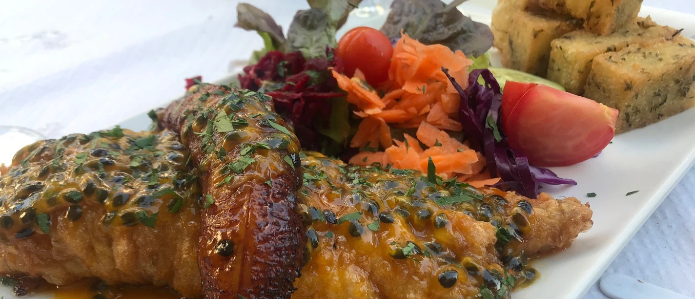 Fischteller Gericht mit gebratenem Fisch in Passionsfruchtsauce, Salatbeilage, Kochbanane und gebratenem Brotwürfel.