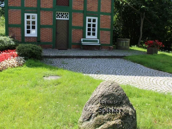 Ein traditionelles Fachwerkgebäude mit roten Backsteinen und grünen Rahmen, umgeben von Natur.