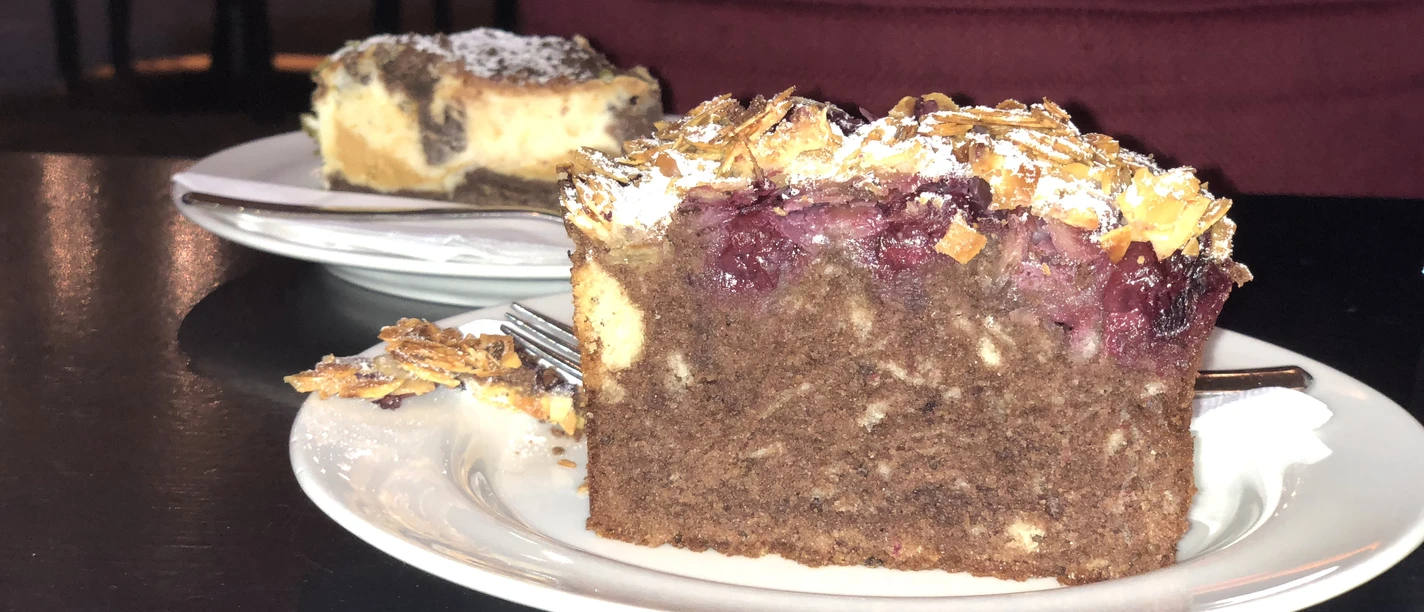 Tortenstück Ein Tortenstück auf einem weißen Teller, verziert mit Kirschen und Mandeln auf dunklem Teig.