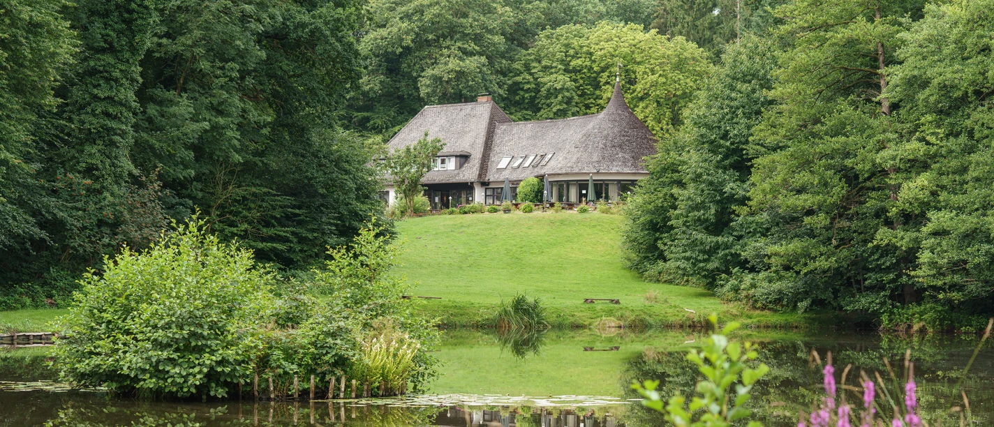 The Wingst Forest House, perched on a green hill, is picturesquely reflected in the tranquil forest lake.