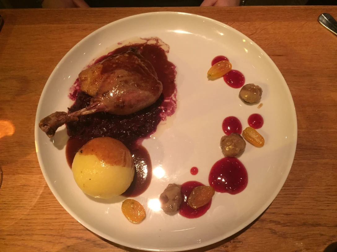 Gans Ein sorgfältig angerichtetes Gericht mit gebratener Gans auf Rotkraut, Kroketten und einer Beilagen-Sauce.