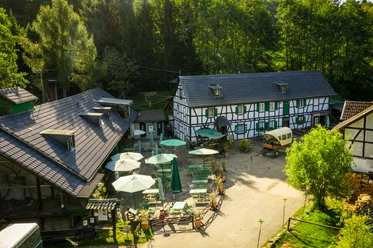 Gammersbacher Mühle Fachwerkhaus mit Biergarten in grüner Umgebung bei Sonnenschein, lädt zum Verweilen ein.