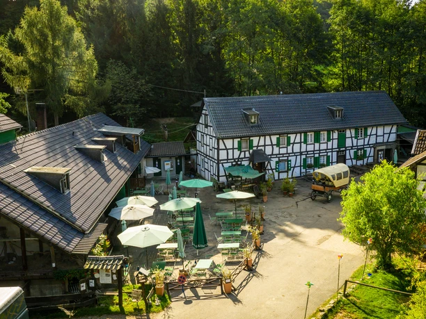 Gammersbacher Mühle Fachwerkhaus mit Biergarten in grüner Umgebung bei Sonnenschein, lädt zum Verweilen ein.