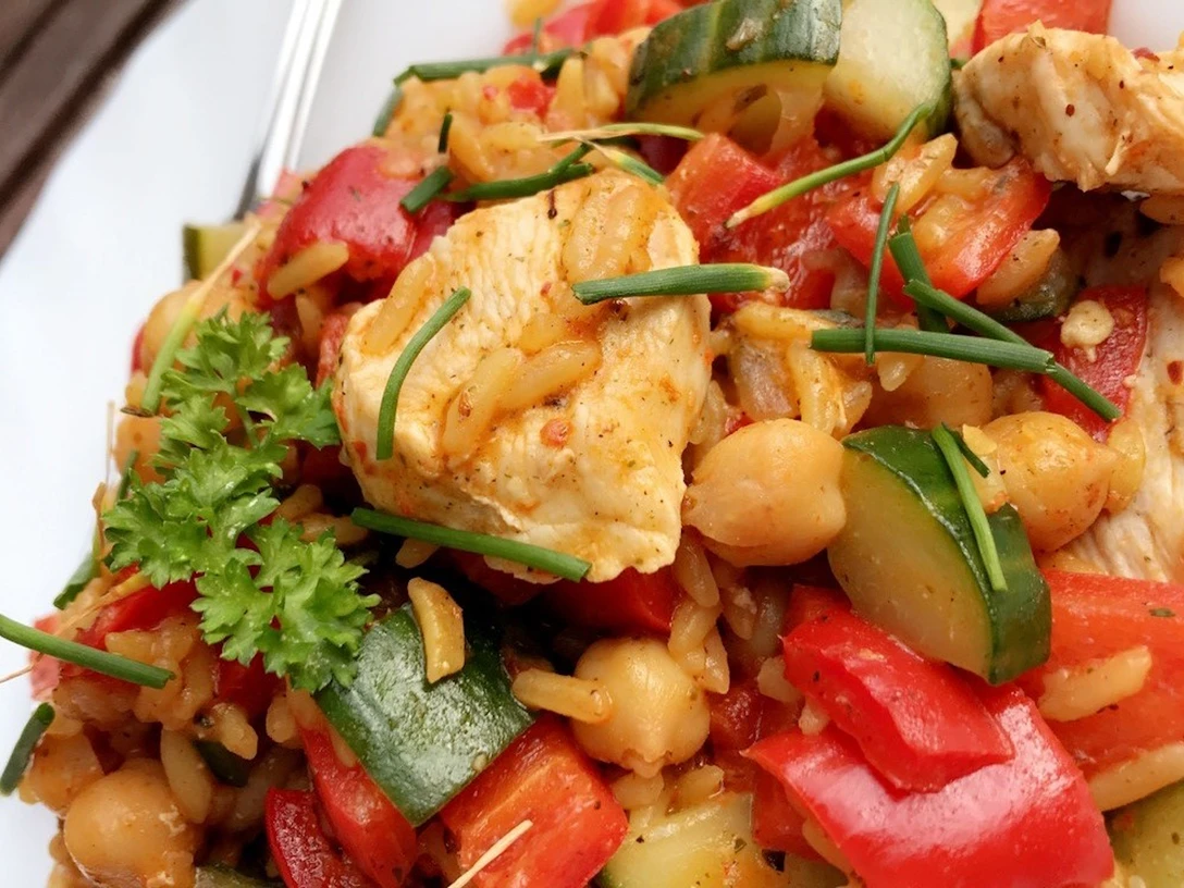 Frisches Hähnchenstück mit knackigem Paprika, Zucchini, Kichererbsen und Reis, garniert mit Schnittlauch.