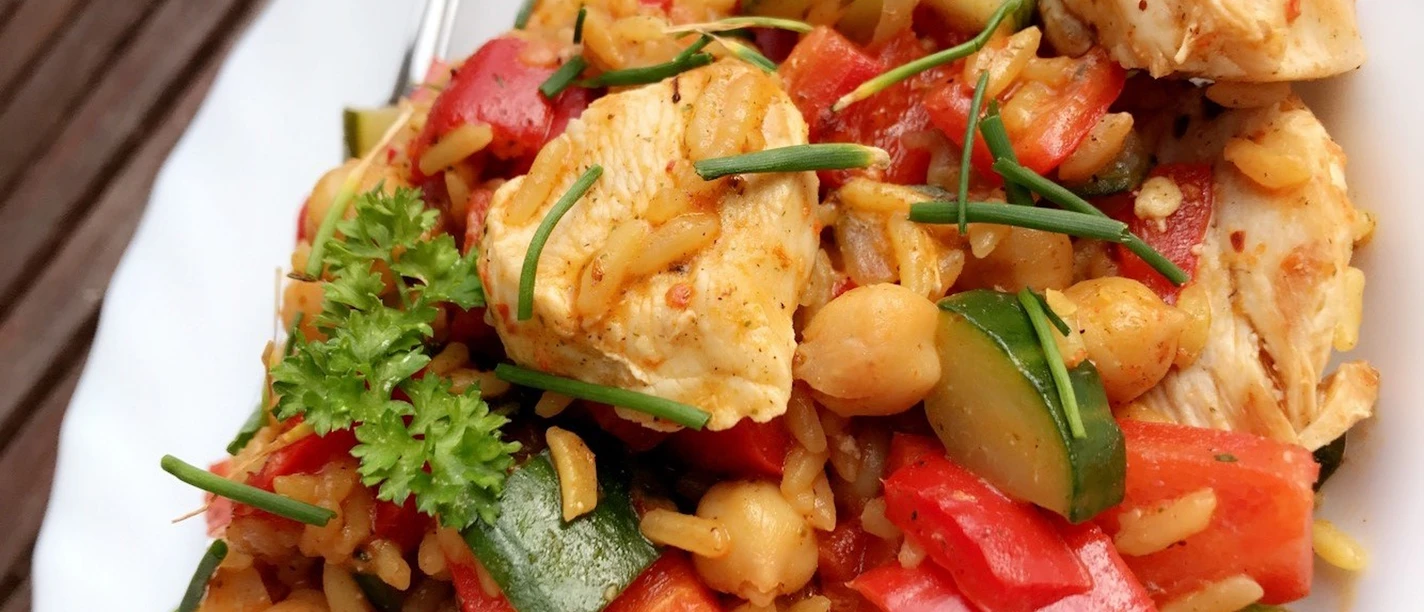 Fresh chicken with crunchy peppers, zucchini, chickpeas and rice, garnished with chives.