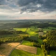 Reichshof Blockhaus Luftaufnahme einer grünen, hügeligen Landschaft bei Reichshof unter bewölktem Himmel im Abendlicht.