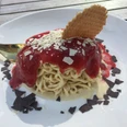 Spaghetti-Eis Spaghetti-Eis mit Erdbeersoße, weißer und dunkler Schokolade sowie einer Waffel auf einem Teller.