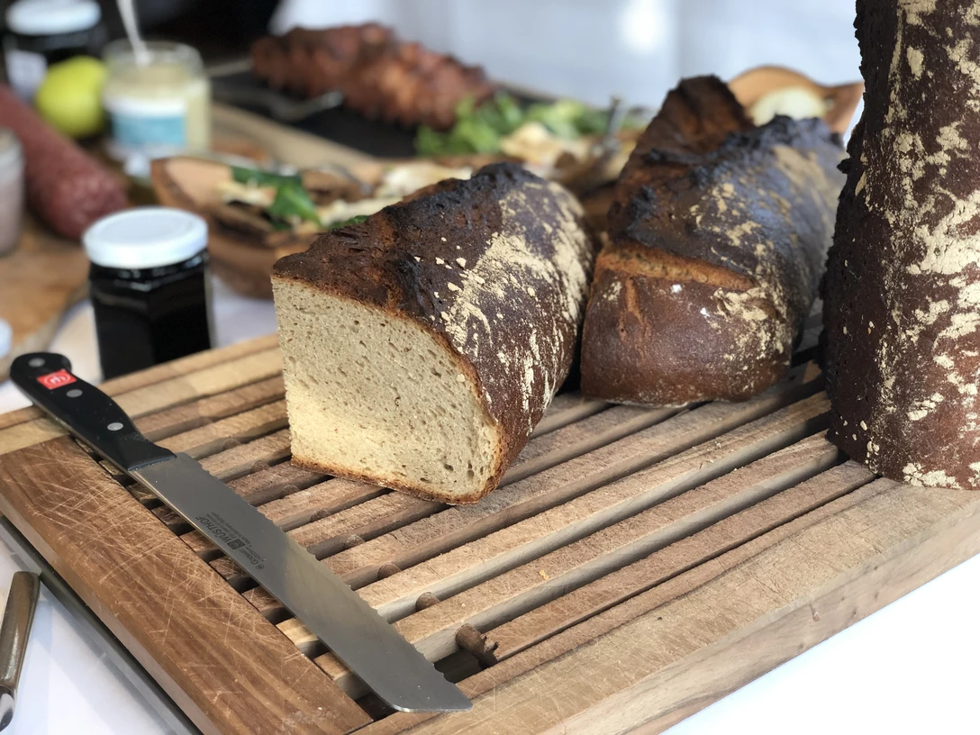 Kalte Platte Verschiedene Brotsorten auf einem rustikalen Holzbrett, flankiert von einem Messer im Vordergrund.
