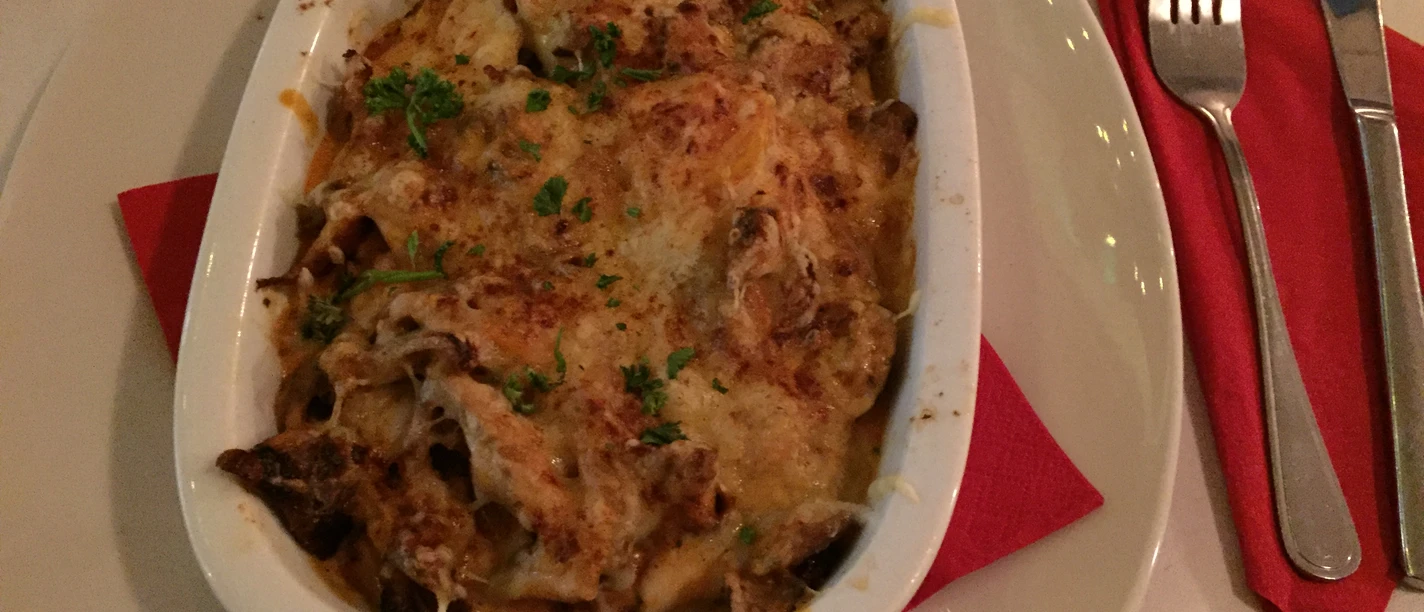 Griechischer Teller Vollmundiges Gratin aus der griechischen Küche, angerichtet mit frischen Kräutern und geschmolzenem Käse.