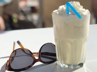 Milchshake Ein erfrischender Milchshake mit Sahnehaube und blauem Strohhalm steht neben einer Sonnenbrille.