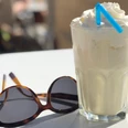 Milchshake Ein erfrischender Milchshake mit Sahnehaube und blauem Strohhalm steht neben einer Sonnenbrille.