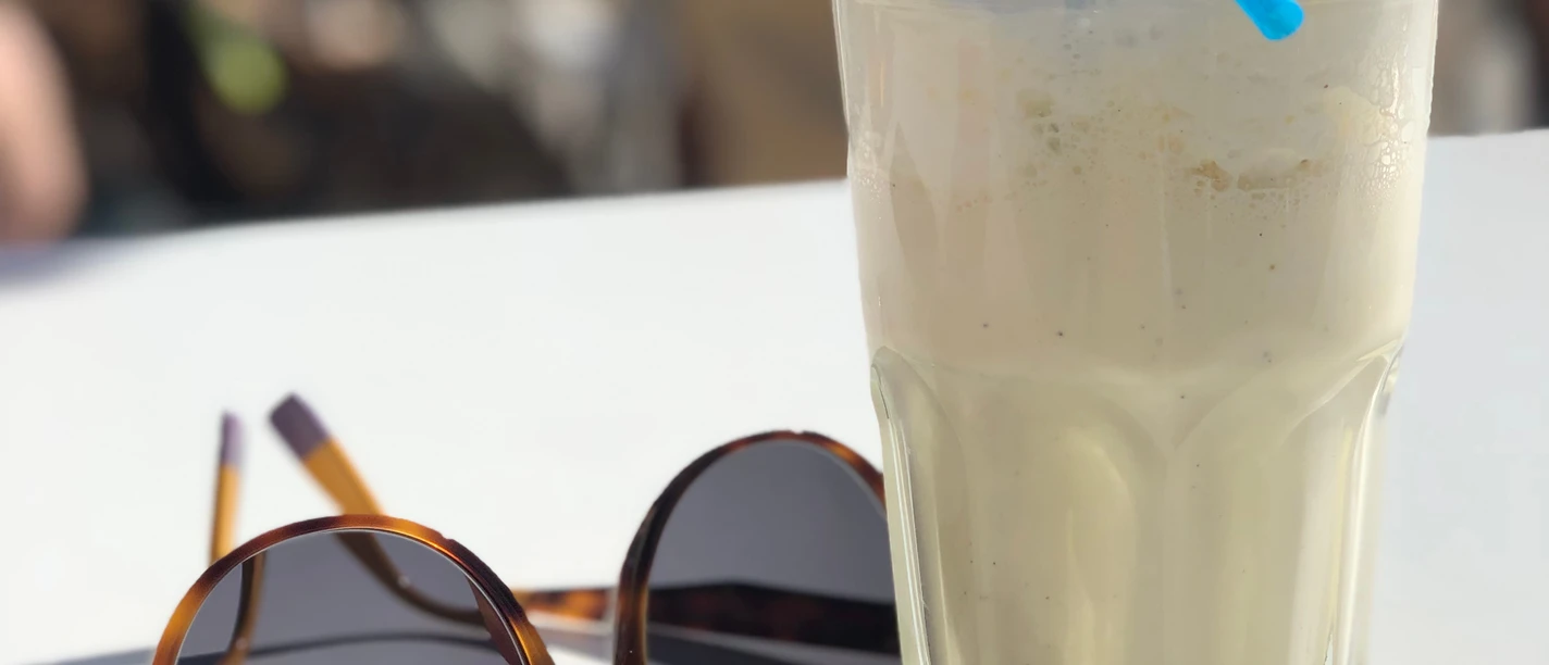 Milchshake Ein erfrischender Milchshake mit Sahnehaube und blauem Strohhalm steht neben einer Sonnenbrille.