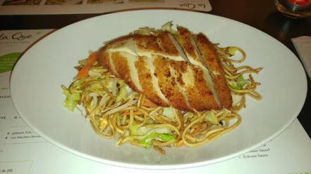 Krokant gebakken kipfilet rust op pittig gebakken Chinese noedels met verse groenten.