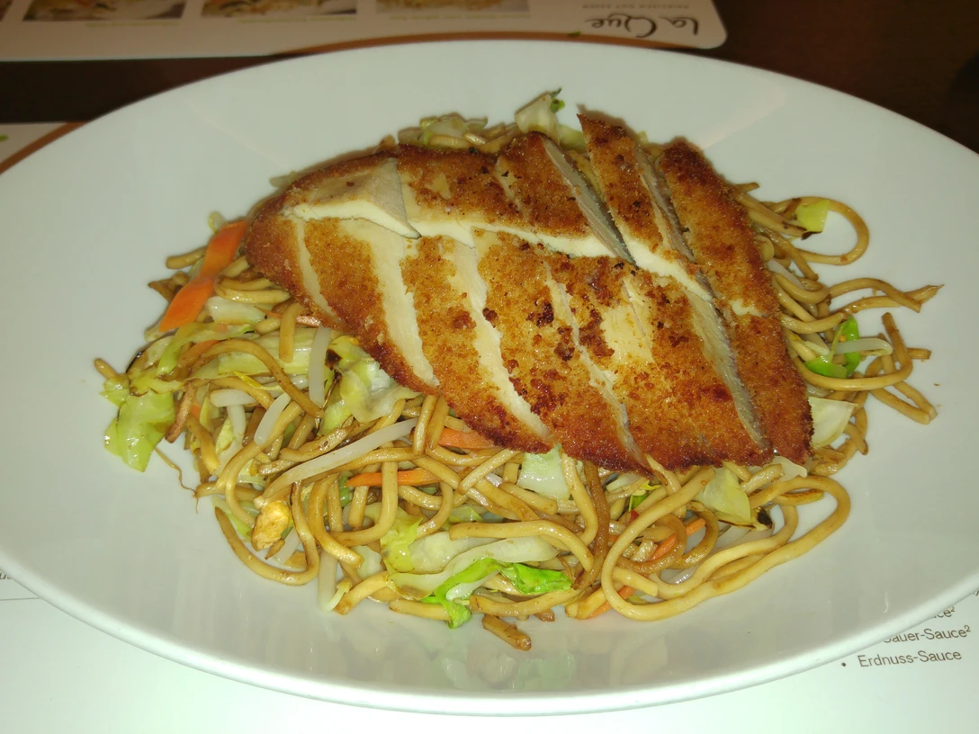 Hähnchenbrust, knusprig gebraten, ruht auf würzig gebratenen Chinanudeln mit frischem Gemüse.