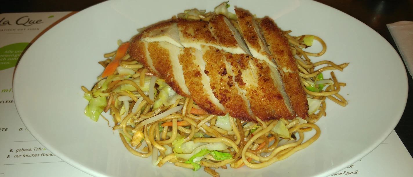 Crispy fried chicken breast rests on spicy fried Chinese noodles with fresh vegetables.