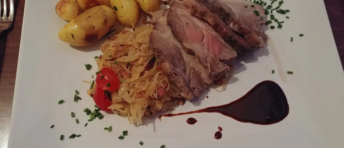 Een bord met sappige plakjes varkensvlees, zuurkool, geroosterde aardappelen en een balsamicosausje.