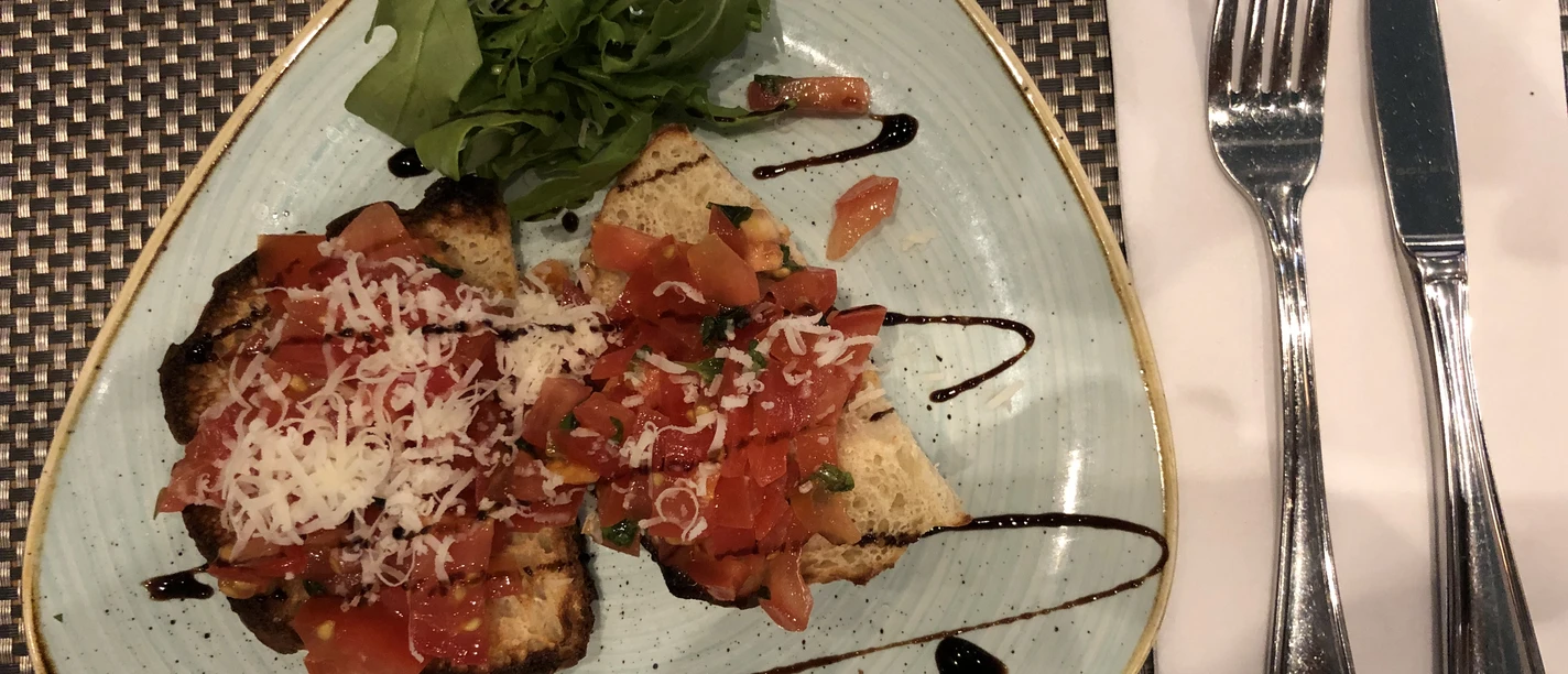 Een driehoekig bord bruschetta belegd met verse tomaten, kaas, kruiden en balsamicoazijn.