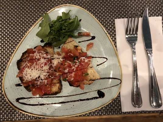 Ein Dreiecksteller mit Bruschetta, belegt mit frischen Tomaten, Käse, Kräutern und Balsamico.