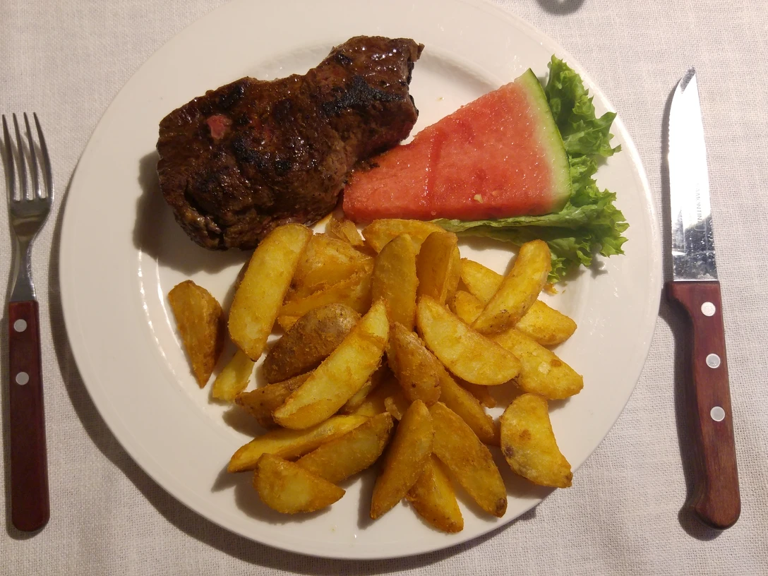 Steakteller Saftiges Steak mit frisch goldenen Kartoffelspalten und erfrischender Wassermelone auf einem Teller.Juicy steak with fresh golden potato wedges and refreshing watermelon on a plate.Saftig bøf med friske, gyldne kartoffelbåde og forfriskende vandmelon på en tallerken.Sappige steak met verse gouden aardappelpartjes en verfrissende watermeloen op een bord.