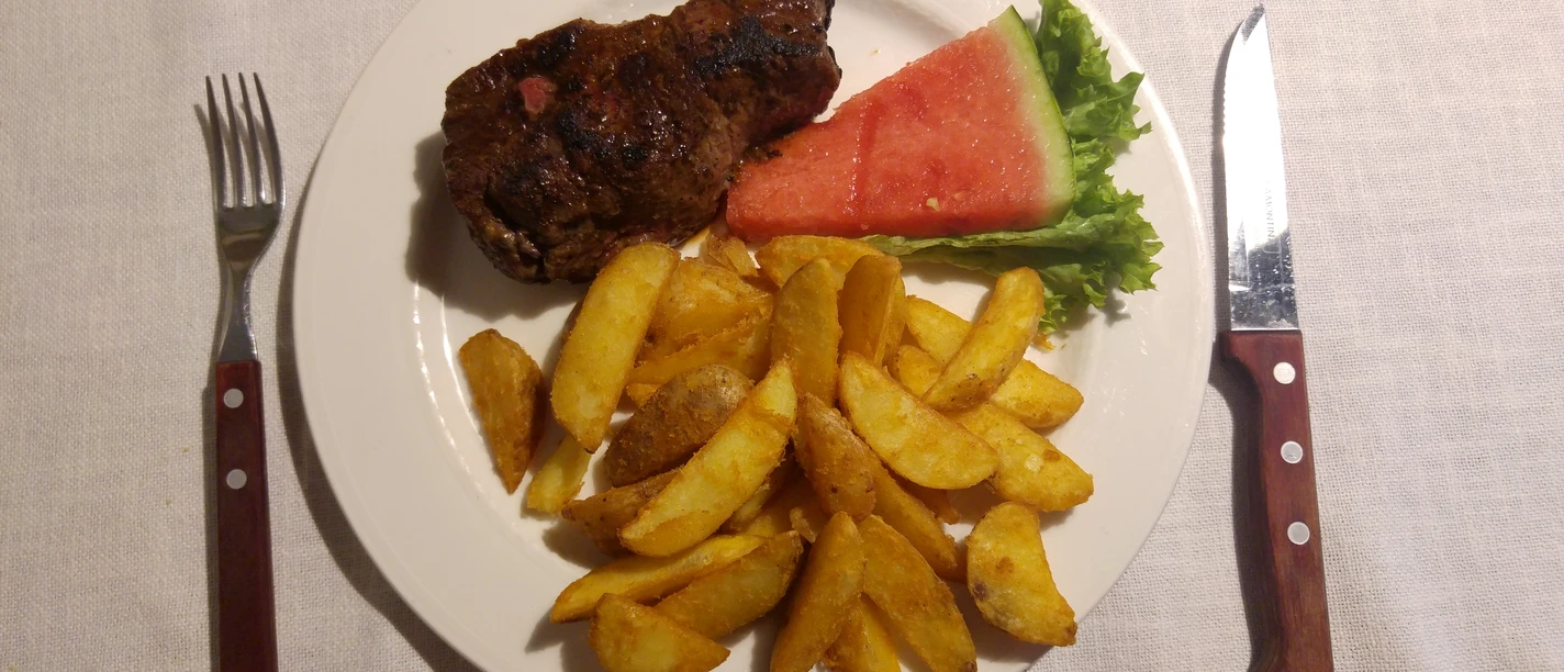 Steakteller Saftiges Steak mit frisch goldenen Kartoffelspalten und erfrischender Wassermelone auf einem Teller.