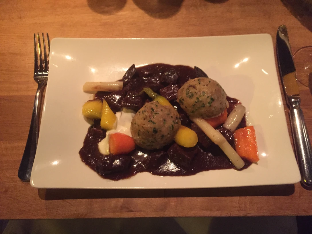 Zwei Semmelknödel mit Gemüse und einer dunklen Sauce präsentieren sich auf einem weißen Teller.