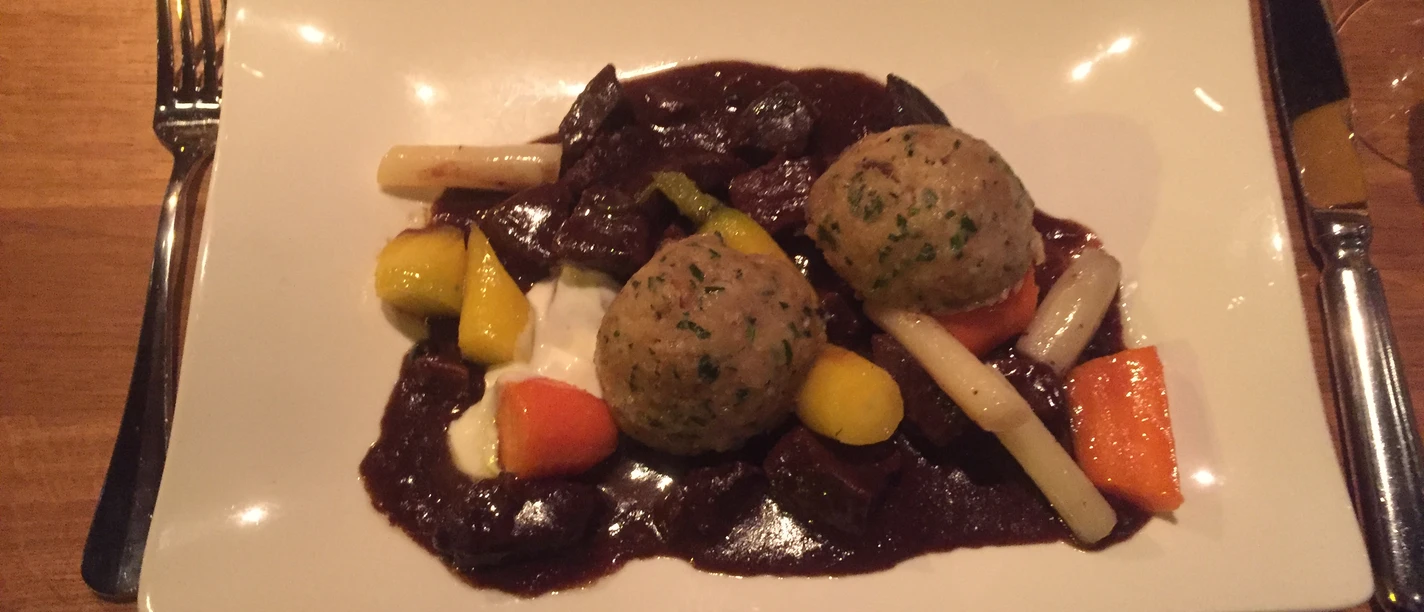 Hauptspeise Zwei Semmelknödel mit Gemüse und einer dunklen Sauce präsentieren sich auf einem weißen Teller.