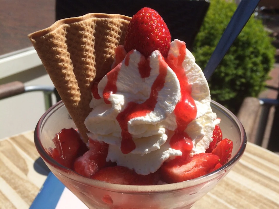 Ice cream sundae with whipped cream, fresh strawberries, waffles and red sauce served in a glass bowl.