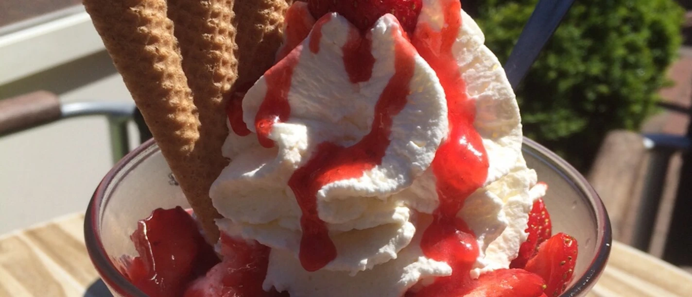 Ice cream sundae with whipped cream, fresh strawberries, waffles and red sauce served in a glass bowl.
