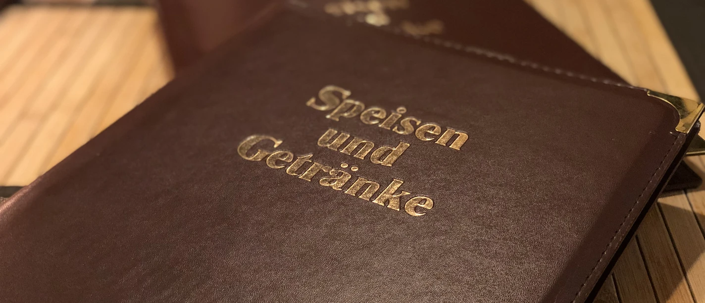 Speisekarte Nahaufnahme eines dunkelbraunen Leder-Speisekartenordners mit goldener Prägung "Speisen und Getränke".