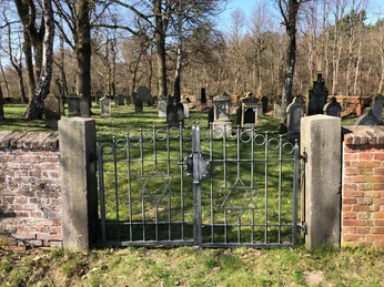 Jüdischer Friedhof Liebenau Ein historischer Friedhof mit schmiedeeisernem Tor, das zwei Davidsterne zeigt, umgeben von Grabsteinen.