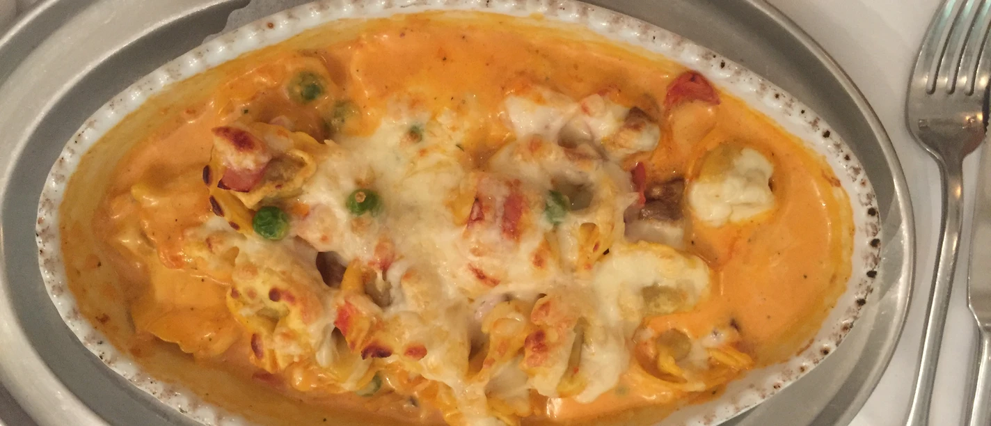 An oval plate of gratinated pasta covered with vegetables and melted cheese.