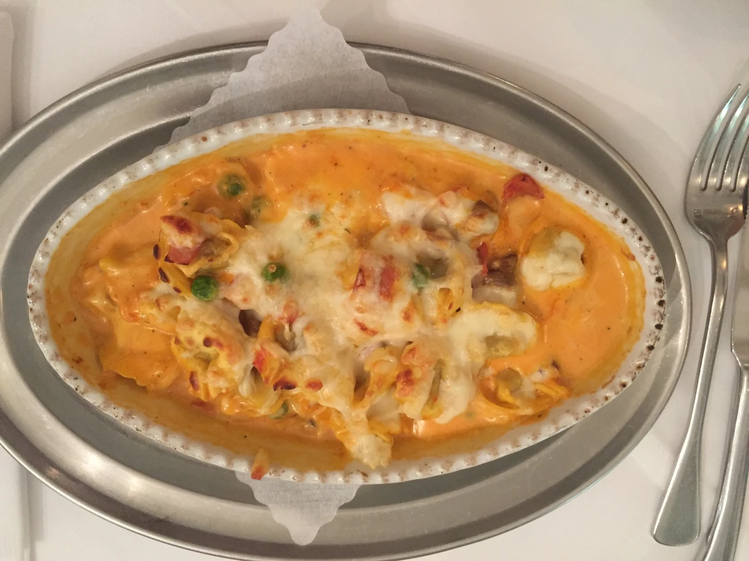 Nudelgericht Ein ovaler Teller mit überbackener Pasta, bedeckt mit Gemüse und geschmolzenem Käse.