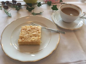 Een mooi gedekte tafel met een stuk taart op een bord en een kopje koffie ernaast.