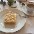 Kaffee + Kuchen Ein fein gedeckter Tisch mit einem Stück Kuchen auf einem Teller und einer Tasse Kaffee daneben.