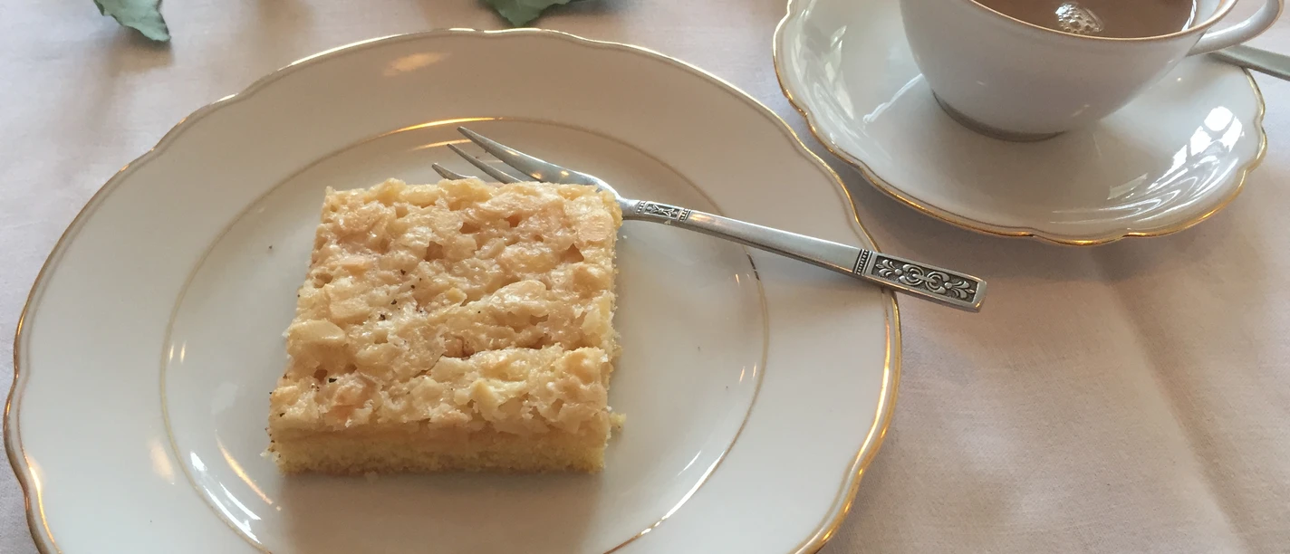 Kaffee + Kuchen Ein fein gedeckter Tisch mit einem Stück Kuchen auf einem Teller und einer Tasse Kaffee daneben.