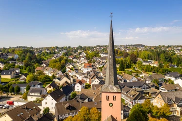 Innenstadt St.-Martinus-Kirche mit spitzem Turm in Much, umgeben von malerischen Fachwerkhäusern und grüner Landschaft.
