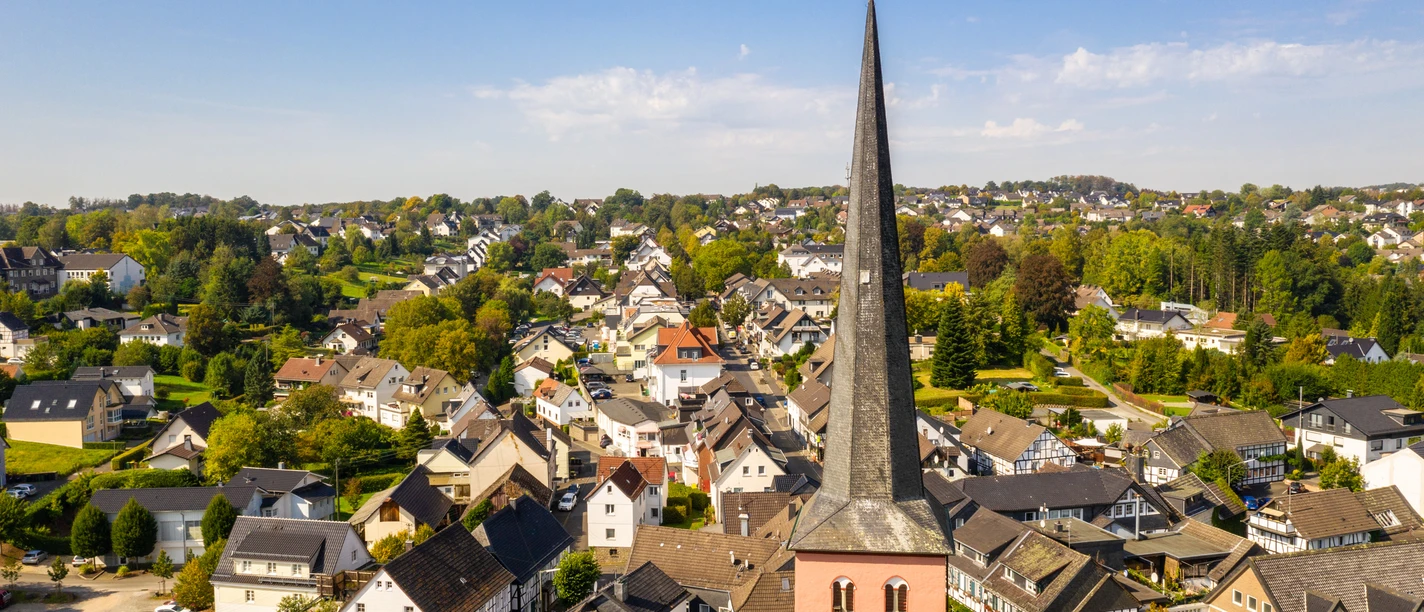 Innenstadt St.-Martinus-Kirche mit spitzem Turm in Much, umgeben von malerischen Fachwerkhäusern und grüner Landschaft.