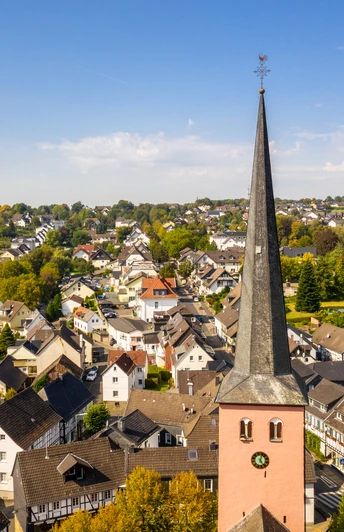 Innenstadt St.-Martinus-Kirche mit spitzem Turm in Much, umgeben von malerischen Fachwerkhäusern und grüner Landschaft.