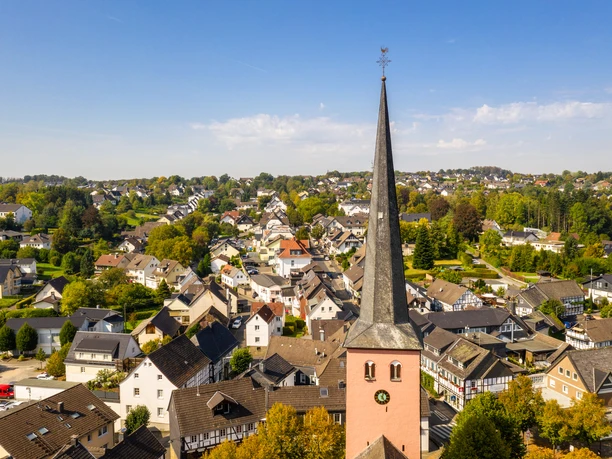 Innenstadt St.-Martinus-Kirche mit spitzem Turm in Much, umgeben von malerischen Fachwerkhäusern und grüner Landschaft.