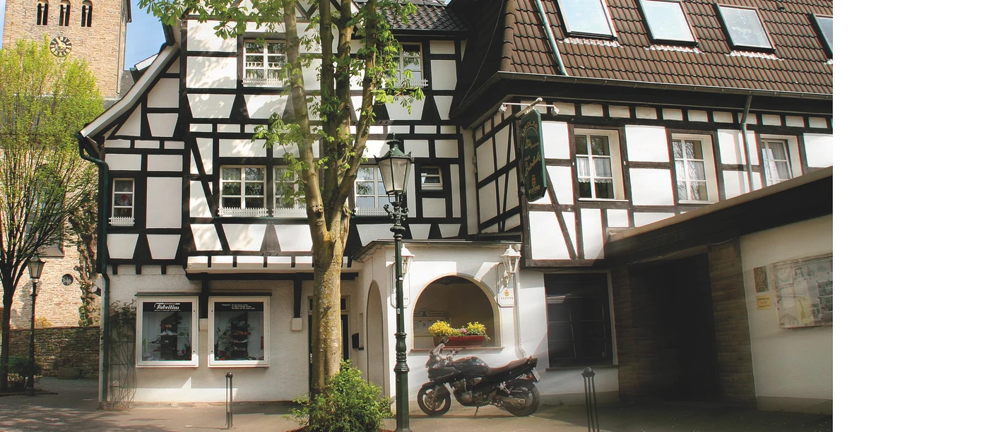 Biesenbach Fachwerkhaus mit Satteldach und angrenzendem Gebäude, davor ein Baum und ein Motorrad.