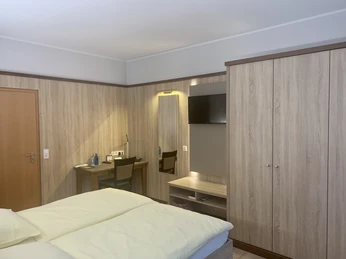 Hotel-Restaurant Lüdenbach Modernes Hotelzimmer mit einem Doppelbett, Holzdekoration, Schreibtisch, Flachbildfernseher und Schrank.
