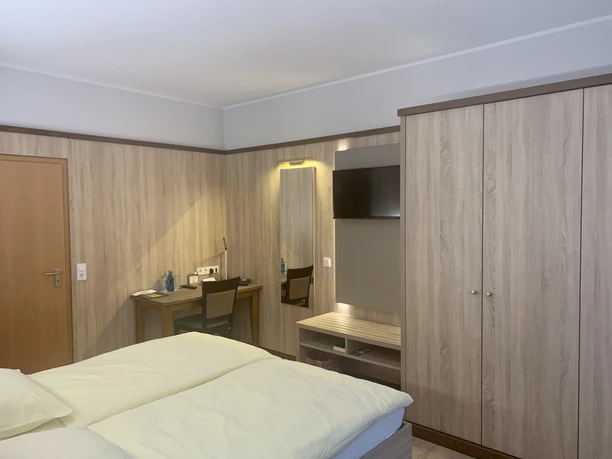 Hotel-Restaurant Lüdenbach Modernes Hotelzimmer mit einem Doppelbett, Holzdekoration, Schreibtisch, Flachbildfernseher und Schrank.
