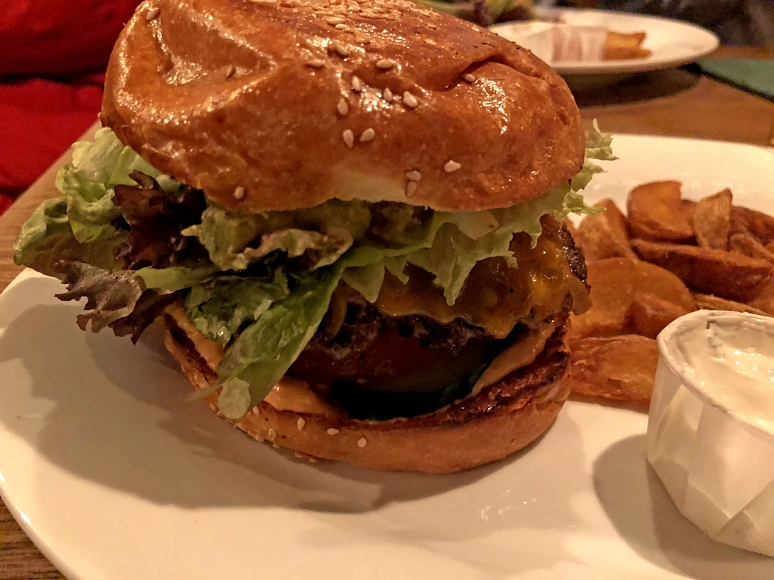 Burger Burger auf Sesambrötchen mit Salatblatt, Käse und Beilage auf einem weißen Teller arrangiert.