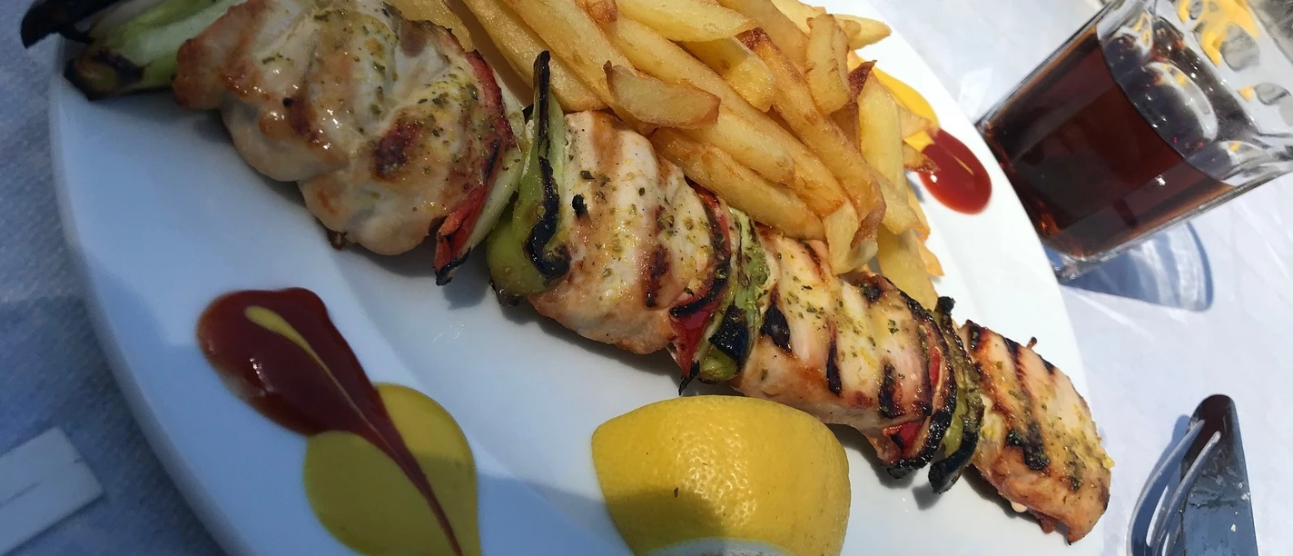 Fleischspieß Gegrillter Fleischspieß mit Paprika und Zwiebeln, serviert mit Pommes frites und Limonenviertel.