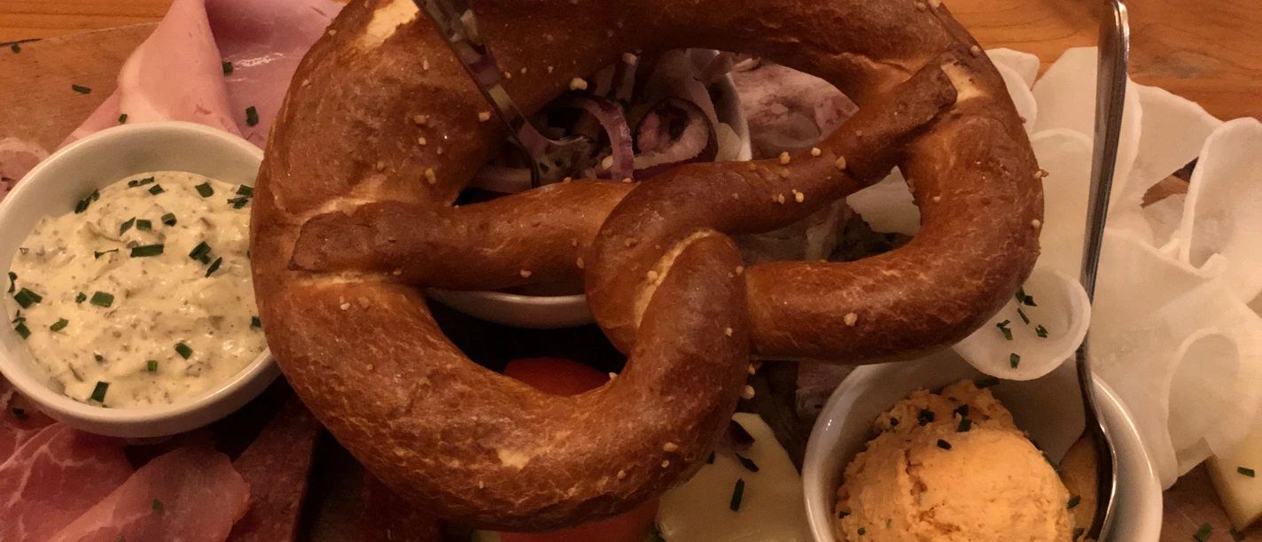 Brezel Herzhafte Brotzeitplatte mit Brezel, regionalen Aufschnitten und Käse, begleitet von würzigen Dips.
