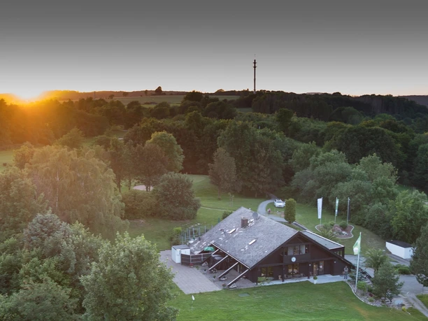 Das Clubhaus liegt malerisch umgeben von üppigem Grün mit sanften Hügeln im Hintergrund.
