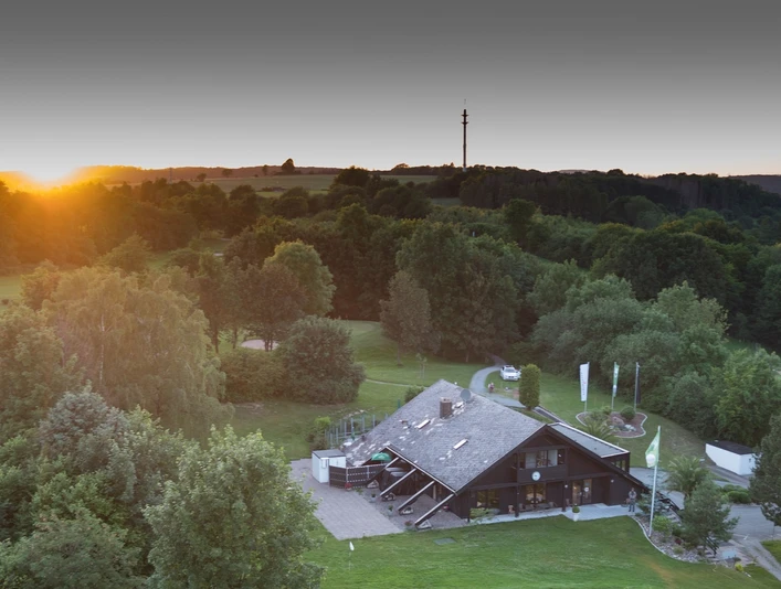 Das Clubhaus liegt malerisch umgeben von üppigem Grün mit sanften Hügeln im Hintergrund.