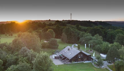 Golfclub Clubhaus Das Clubhaus liegt malerisch umgeben von üppigem Grün mit sanften Hügeln im Hintergrund.