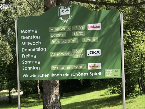 Grüne Infotafel des Golf Clubs Bad Pyrmont mit Spielzeiten und Tagen für After Work und Turniere.
